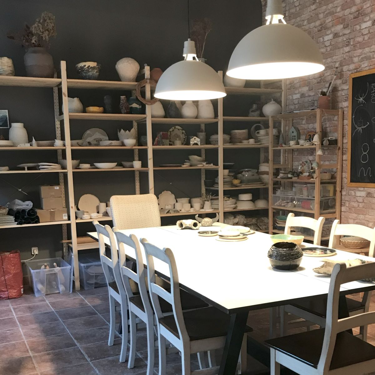 Wnętrze pracowni ceramiki Merence w Warszawie – stół warsztatowy i półki z ręcznie wykonanymi naczyniami