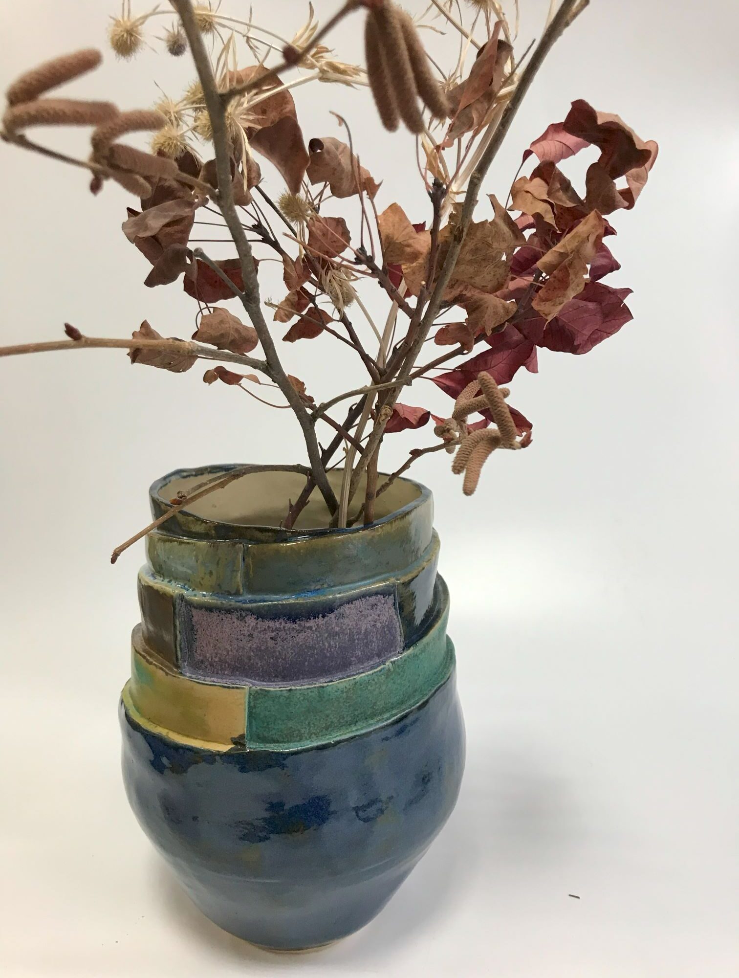 granatowy wazon ceramiczny z wielowarstwowymi szkliwami w odcieniach zieleni, granatu i fioletu.