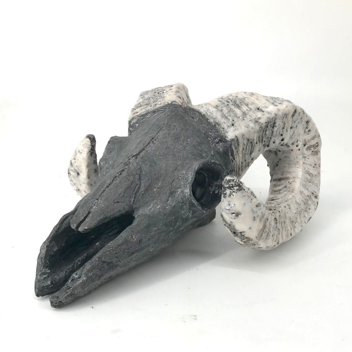 Zdjęcie rzeźby ceramicznej przedstawiającej stylizowaną czaszkę z rogami, wykonanej techniką raku.