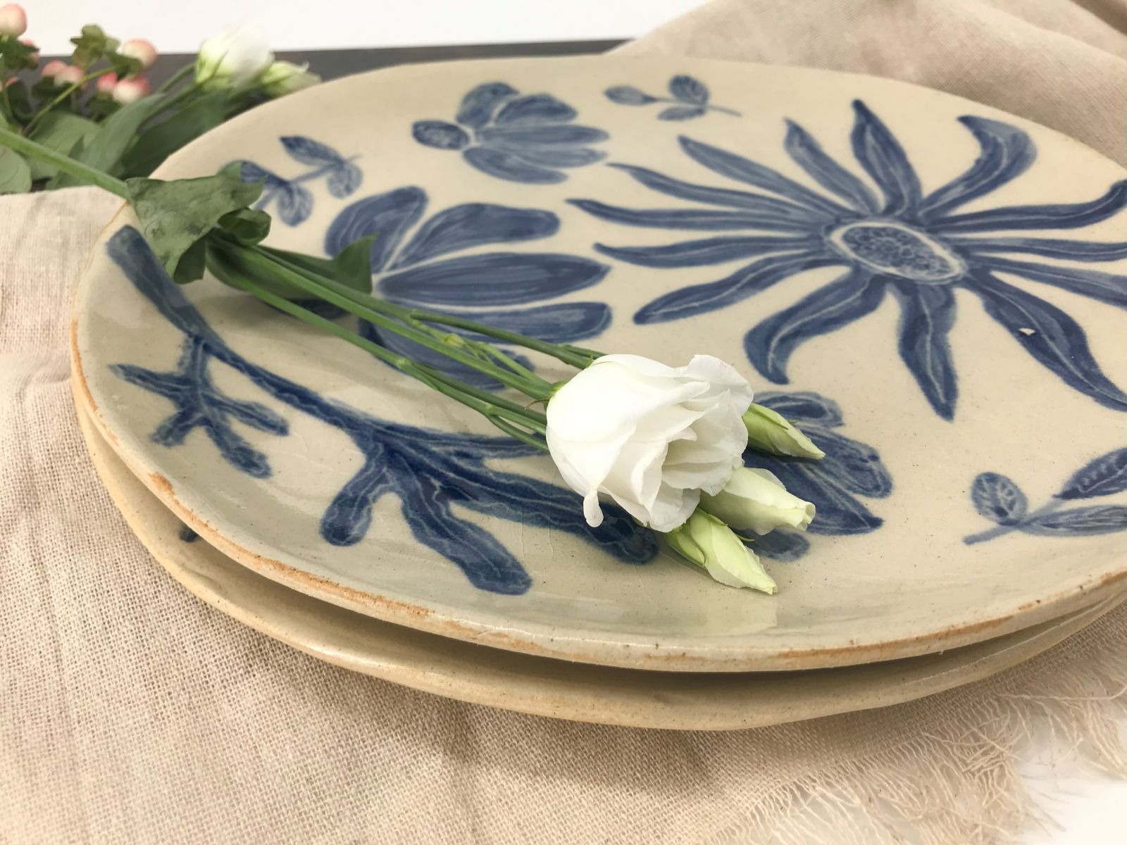 Dwie patery ceramiczne – jedna z kobaltowym wzorem kwiatowym, druga w jednolitym kolorze, ułożone na lnianej tkaninie